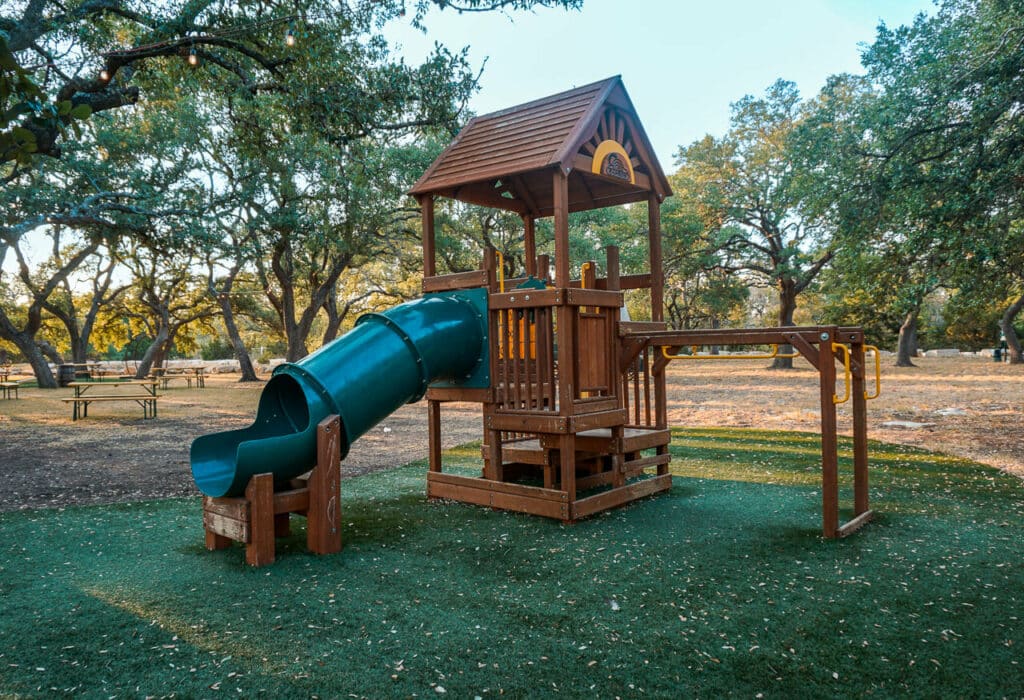 A wooden playground with a green slide located at Dripping Springs Distillery - one of the best kid-friendly distilleries in Dripping Springs.