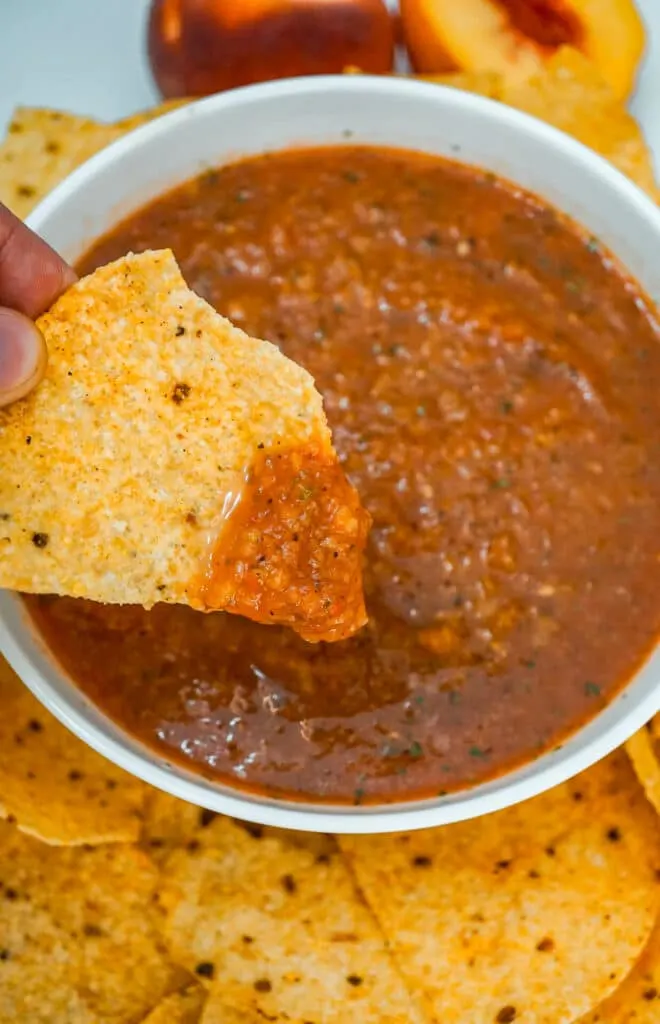 A chip with Grilled Peach Salsa on it above a bowl of salsa. 