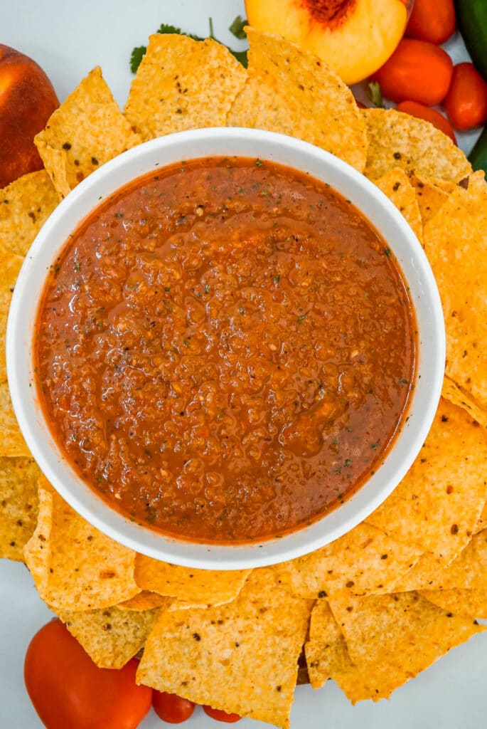 A bowl of Grilled Peach Salsa surrounded by tortilla chips.