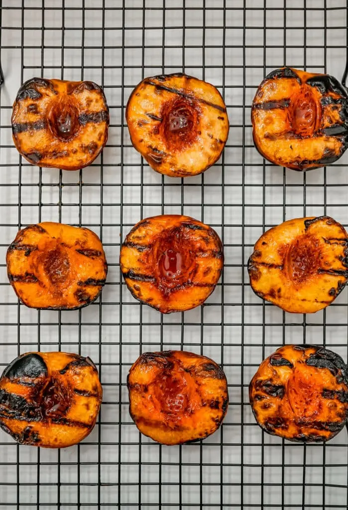 Nine grilled peaches face up on a cooling rack.