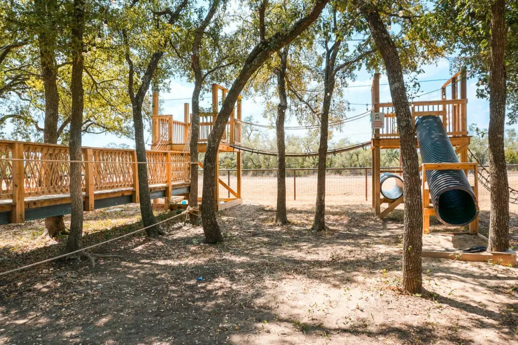An epic wooden fort with a rope bridge and tunnel slide located at One Shot Distillery & Brewery - one of the best kid-friendly distilleries in Dripping Springs. 