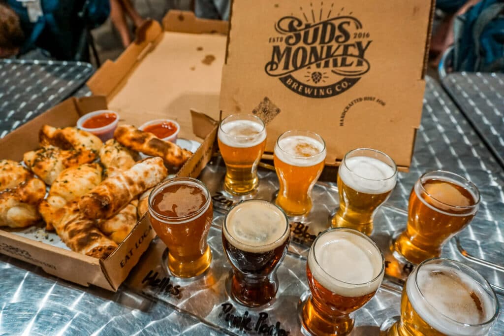 Two beer flights with a box of pizza rolls and a pizza box standing that says Suds Monkey.