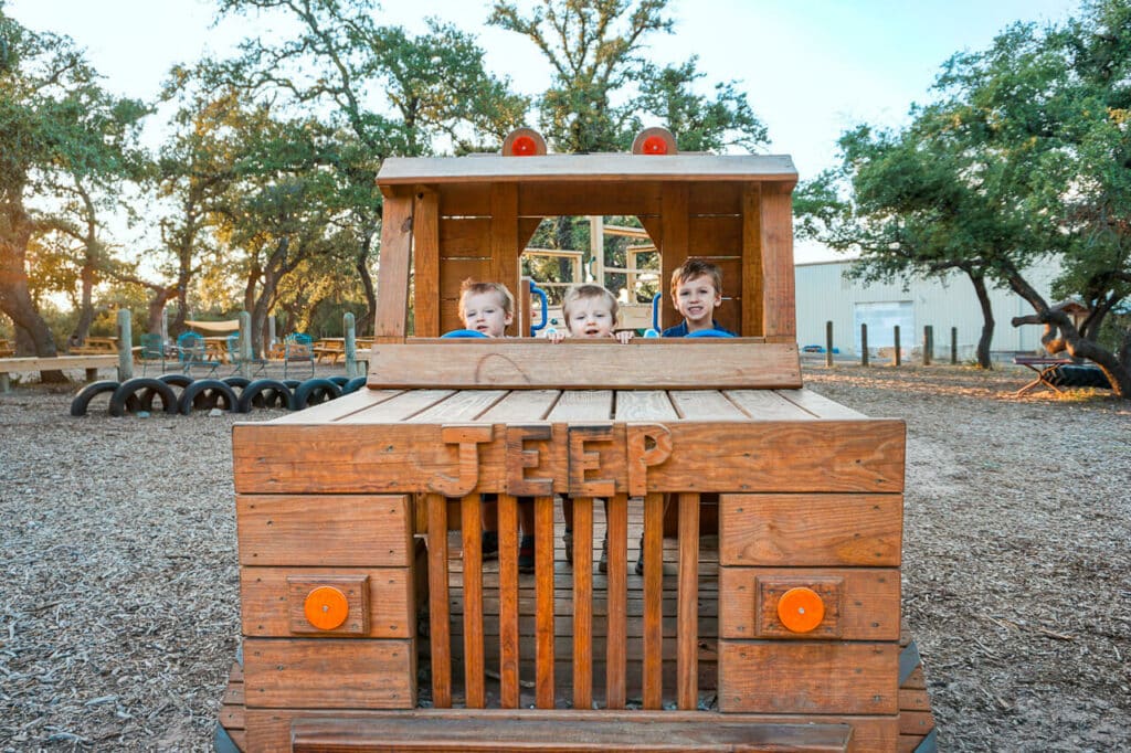 Three toddler boys with their heads barely peeking over a wooden jeep.
