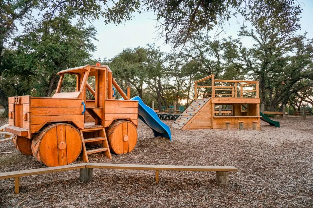 A playground with a wooden jeep, slide, and climbing structure located at Suds Monkey Brewing Co. in Dripping Springs. 