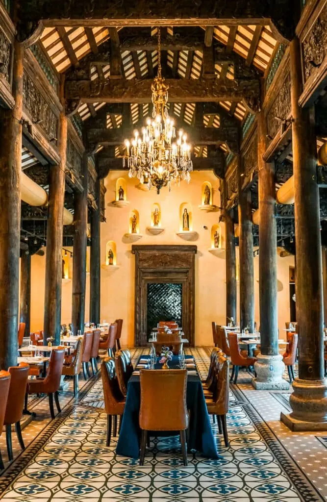 A long dining room table with a chandelier above it inside Tillies restaurant, which is a Vietnamese town hall located at Camp Lucy. 