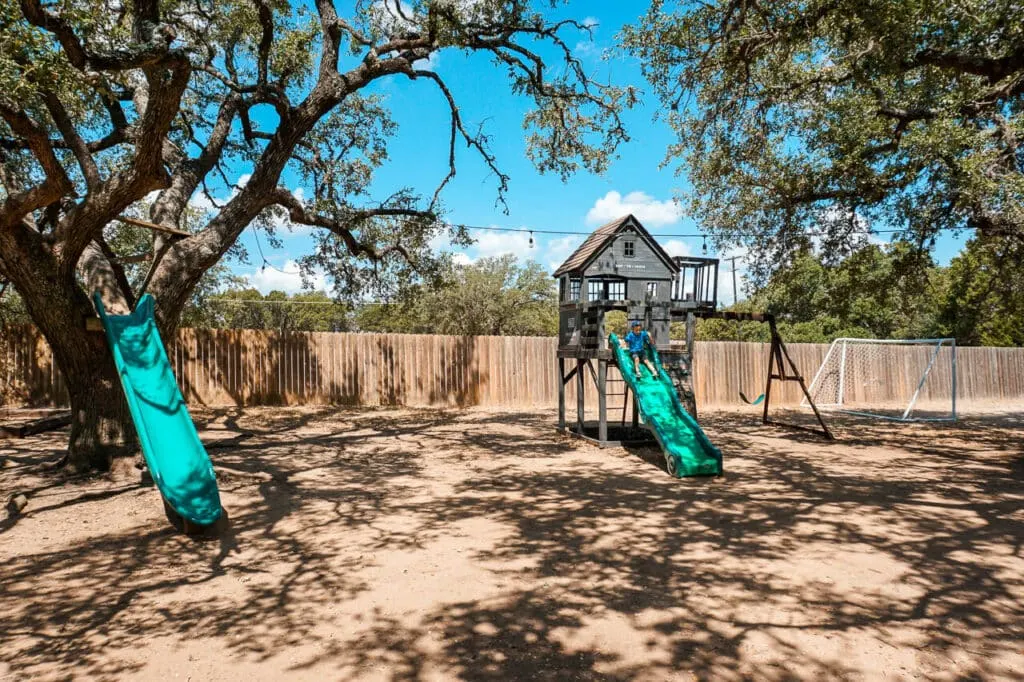 A treehouse slide and wooden playground under the shade of live oak trees at Treaty Oak Distillery - one of the best kid-friendly distilleries in Dripping Springs. 