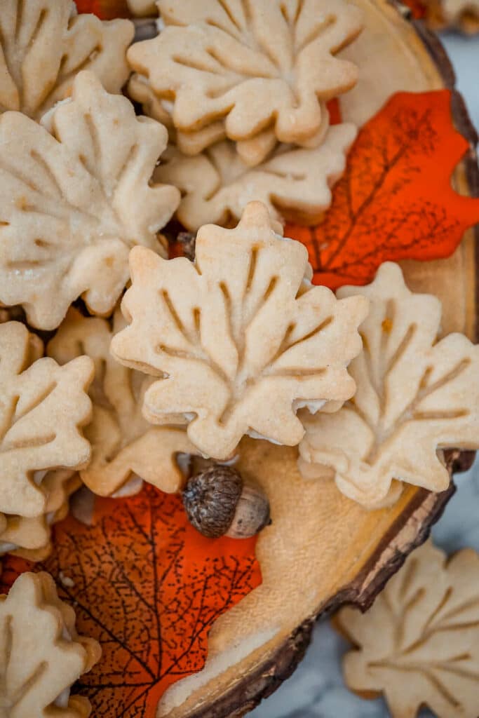 Maple Leaf Cream Sandwich Cookies on a wooden plate with fake red leaves and acorns around the cookies.