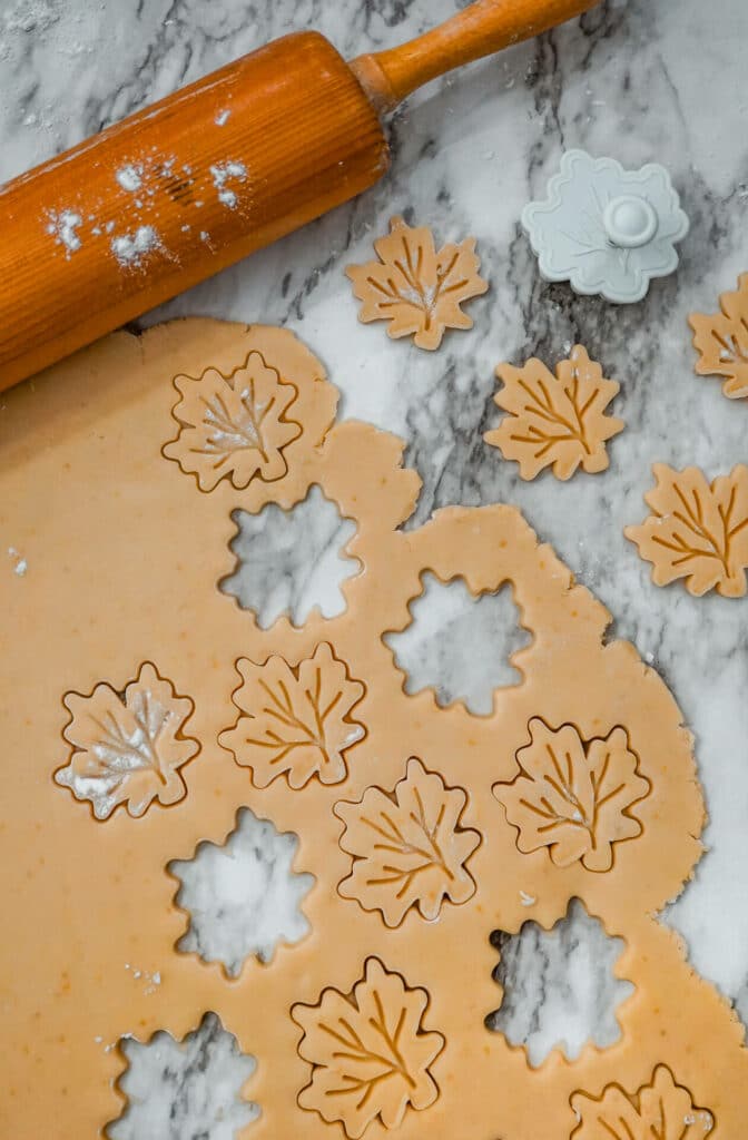 Shortbread cookie dough rolled out with cut outs of a maple leaf and a rolling pin above the dough.