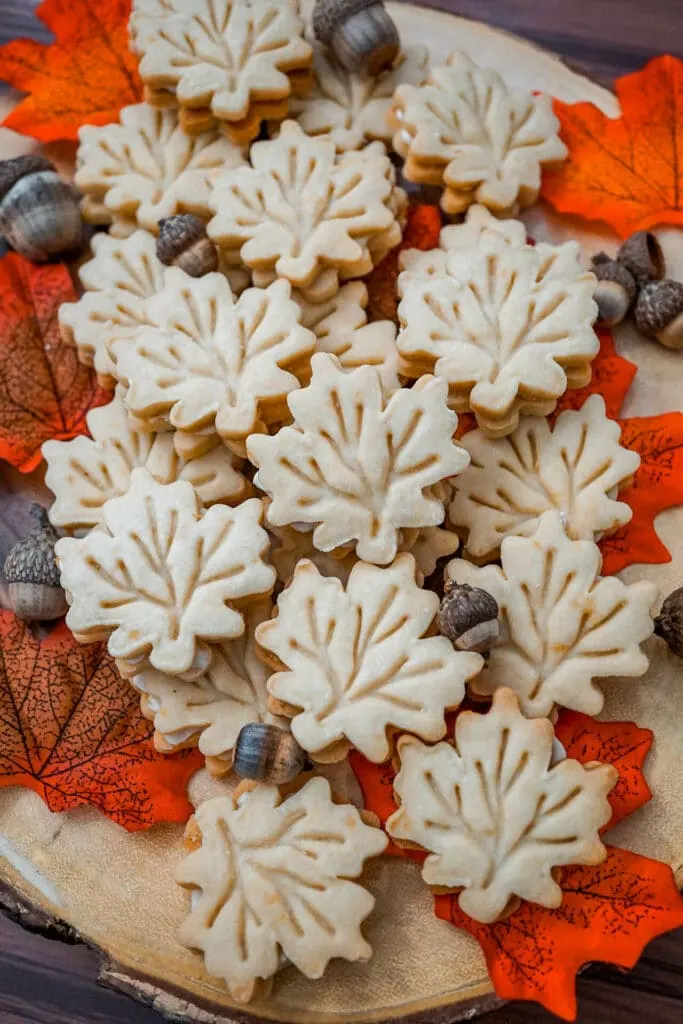 Maple Leaf Cream Cookies on a wooden board with red leaves and acorns surrounding it.