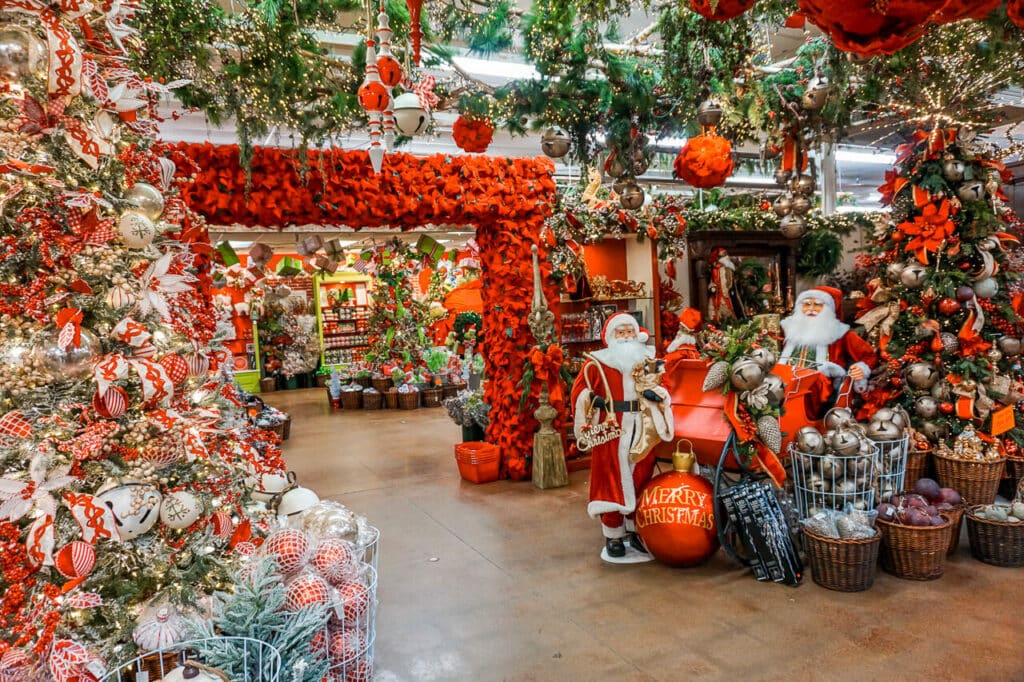 A highly decorated area with  Christmas trees, hanging garland, Santa in a sleigh, and poinsettia arch. Located at The Decorator's Warehouse in Texas.
