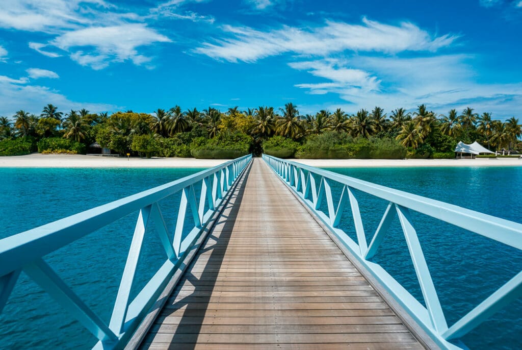 A tropical island in view with a long boardwalk bridge that connects two islands at the Conrad Maldives.