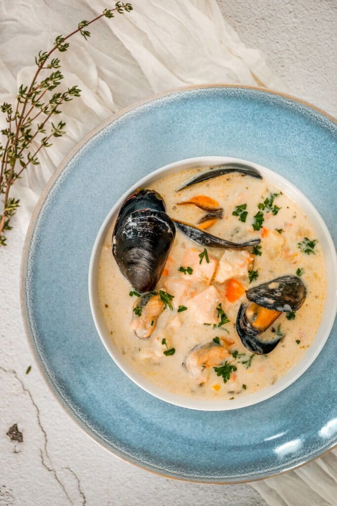 A light blue plate with a bowl of Irish Seafood Chowder with open mussels, chunks of cod, and salmon.