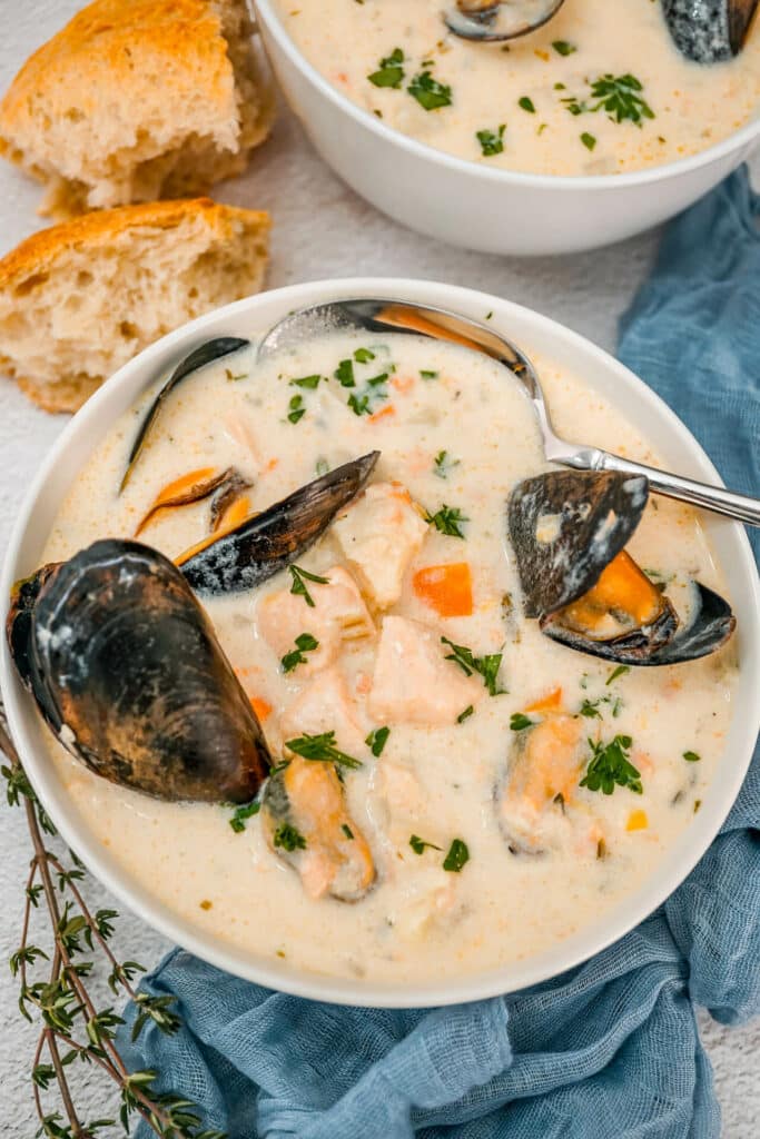 A few pieces of sourdough bread next to a spoon going into a bowl of Irish Seafood Chowder with open mussels, chunks of cod, and salmon.  