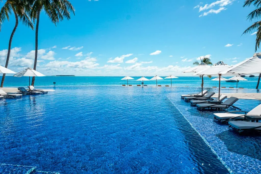 A large infinity pool with several loungers and umbrellas at Conrad Maldives Rangali Island. 