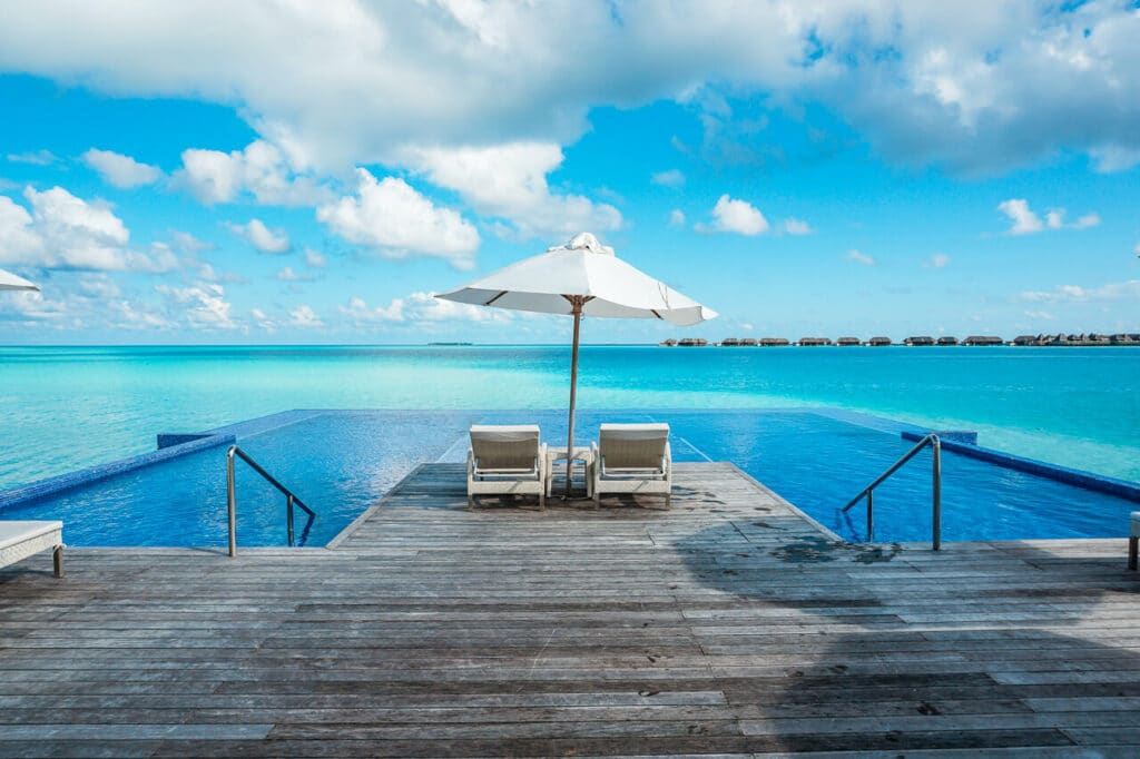 An infinity pool with a sundeck and two loungers under an umbrella at Conrad Maldives Rangali Island.  