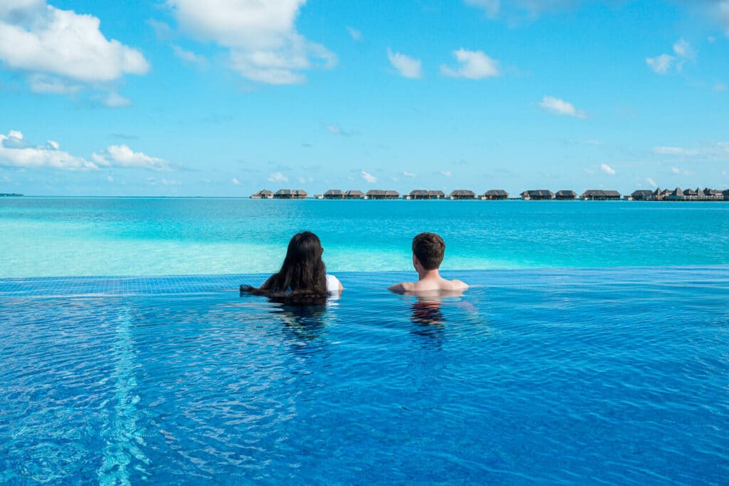 A couple looking out into the turquoise lagoon from an infinity pool at Conrad Maldives Rangali Island.