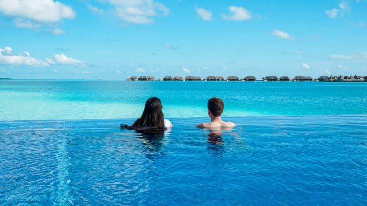 A couple looking out into the turquoise lagoon from an infinity pool at Conrad Maldives Rangali Island.