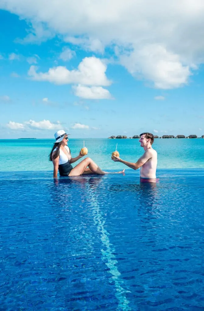 A couple toasting with cocktails in an infinity pool at Conrad Maldives Rangali Island.