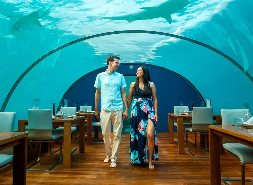 A couple walking in a crystal dome, 16 ft below sea level at Ithaa - the world's first underwater restaurant.