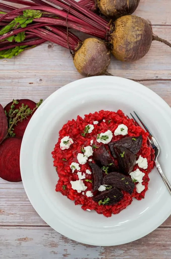 Three fresh red beets and slices of red beets next to Roasted Beet Risotto with Goat Cheese. 