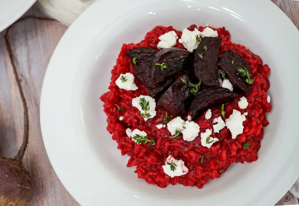 A bowl of Beet Risotto with roasted wedges of beets, goat cheese crumbled on top, and fresh thyme. 