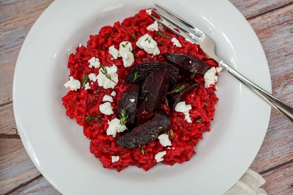 A fork in a bowl of red Roasted Beet Risotto with Goat Cheese crumbled on top and chopped thyme. 