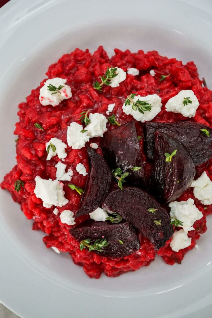 A bowl of red Roasted Beet Risotto with Goat Cheese crumbled on top and chopped thyme. 