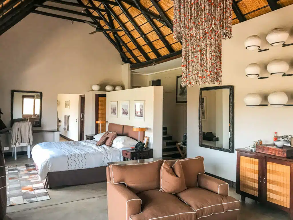 Inside a suite at AndBeyond Phinda Mountain Lodge. The bed faces the window to look out into the reserve, a gorgeous beaded chandelier hangs from the ceiling, and sitting area.
