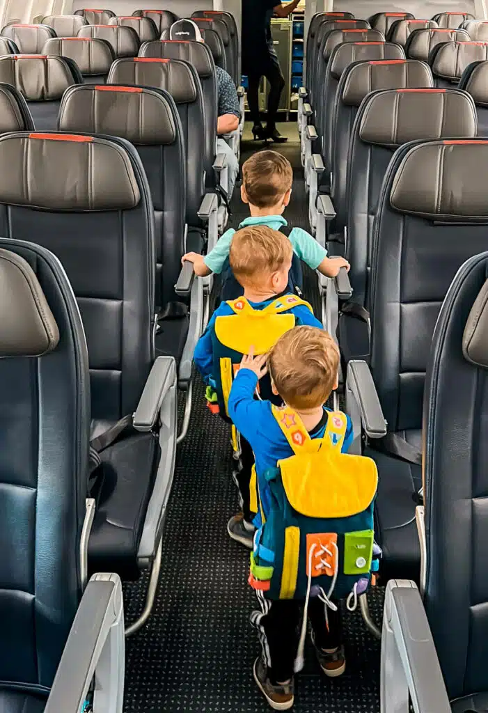 Three toddler boys with backpacks walking down an airport aisle.