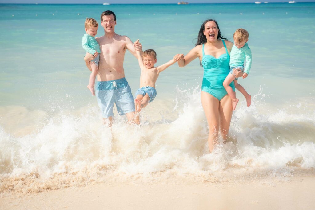 A dad and mom each holding a toddler boy while swimming a young boy in a crystal clear turquoise beach at La Romana.