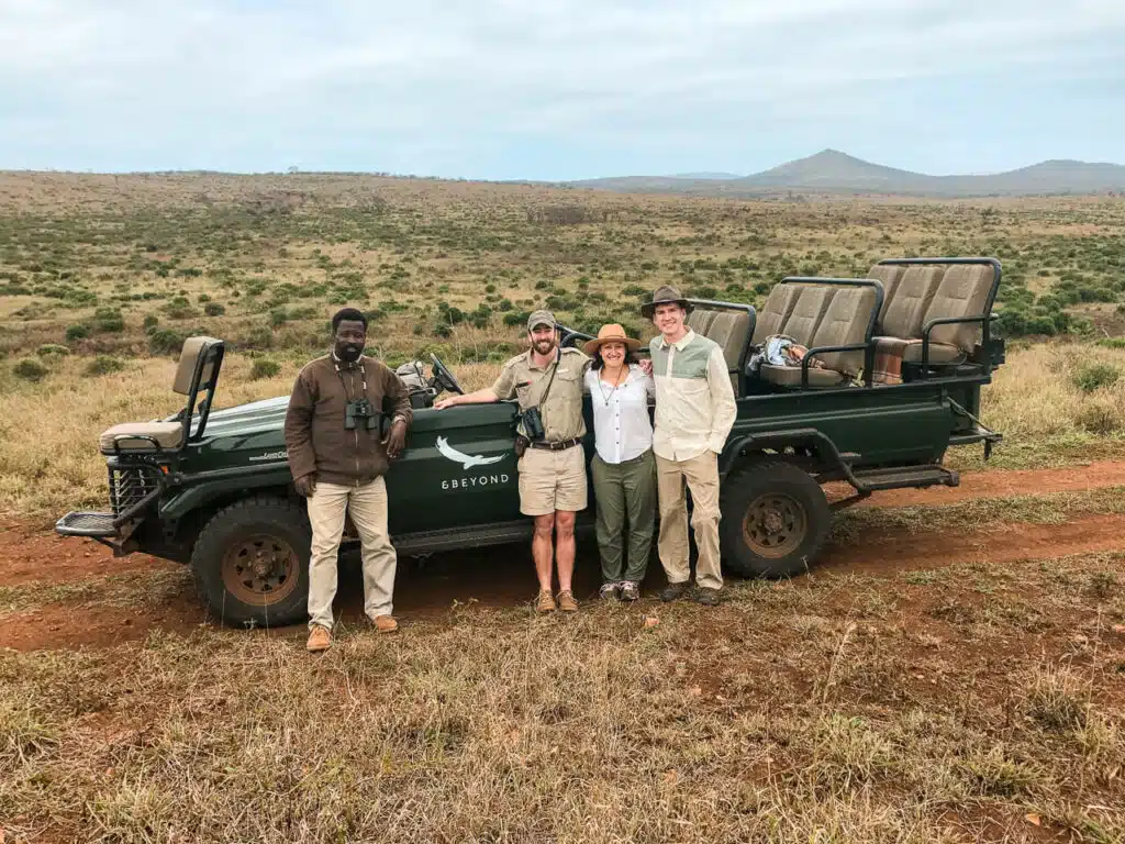 A couple standing with their ranger and tracker in front of a green jeep from AndBeyond Phinda Mountain Lodge.