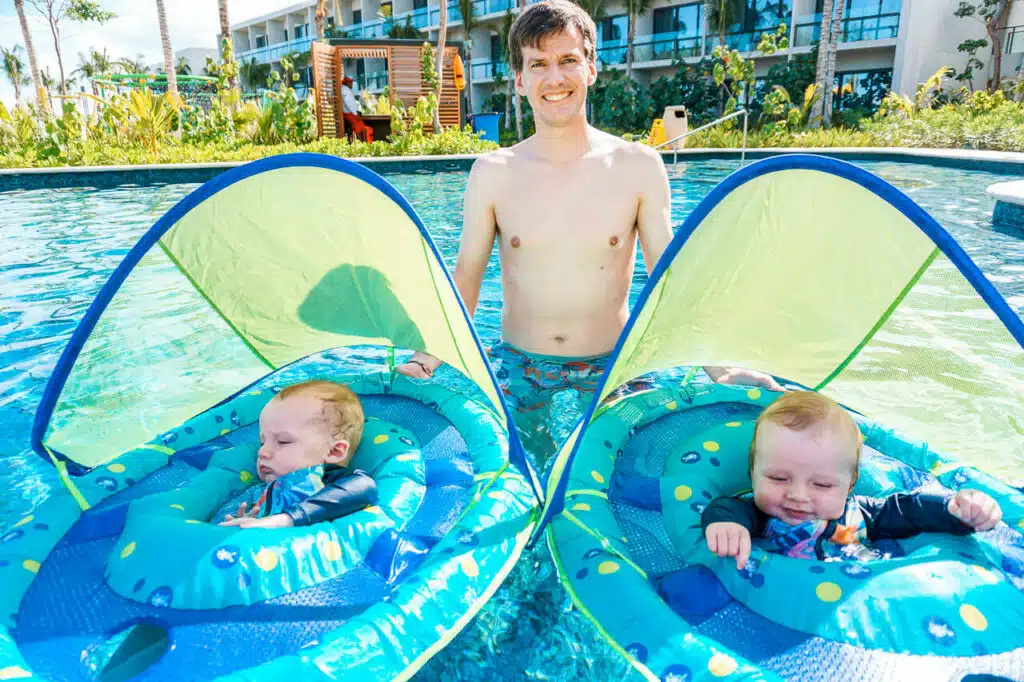 A dad in the pool with his twin boys in swim floats.
