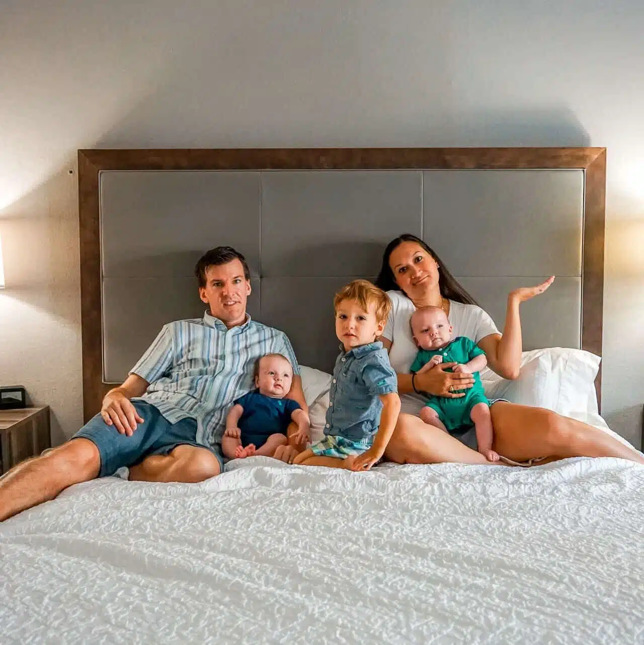 Parents sitting on the bed looking lost traveling with twins and a toddler.