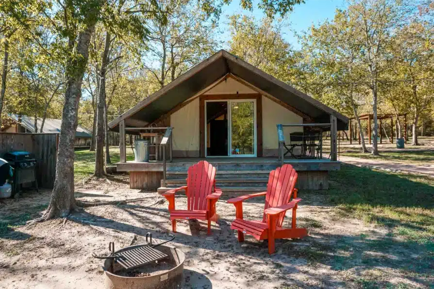 A safari tent with two red chairs next to the campfire at Lake Bastrop North Shore Park.