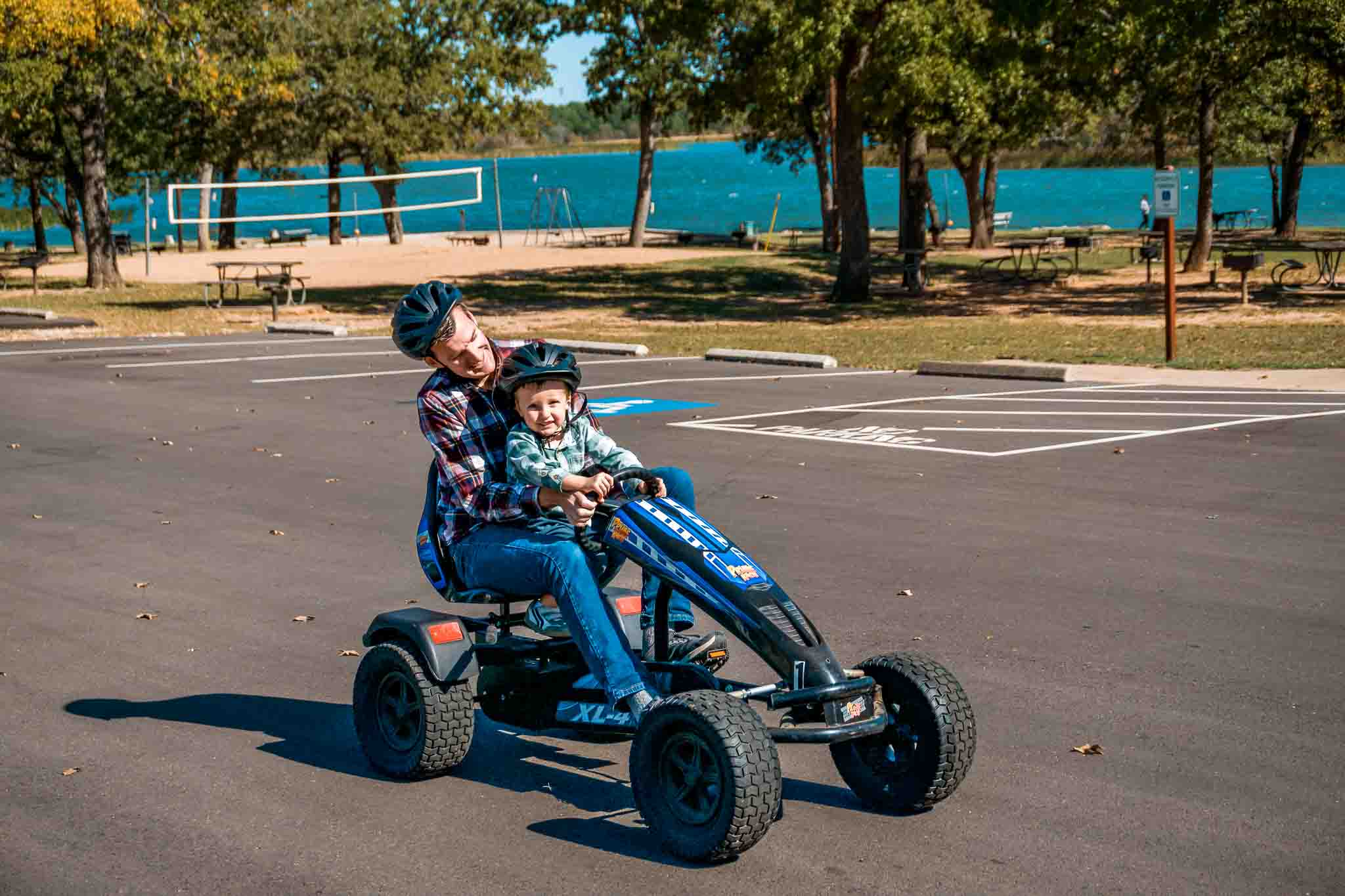 A father and son on a blue pedal cart driving on a parking lot at Lake Bastrop South Shore Park.