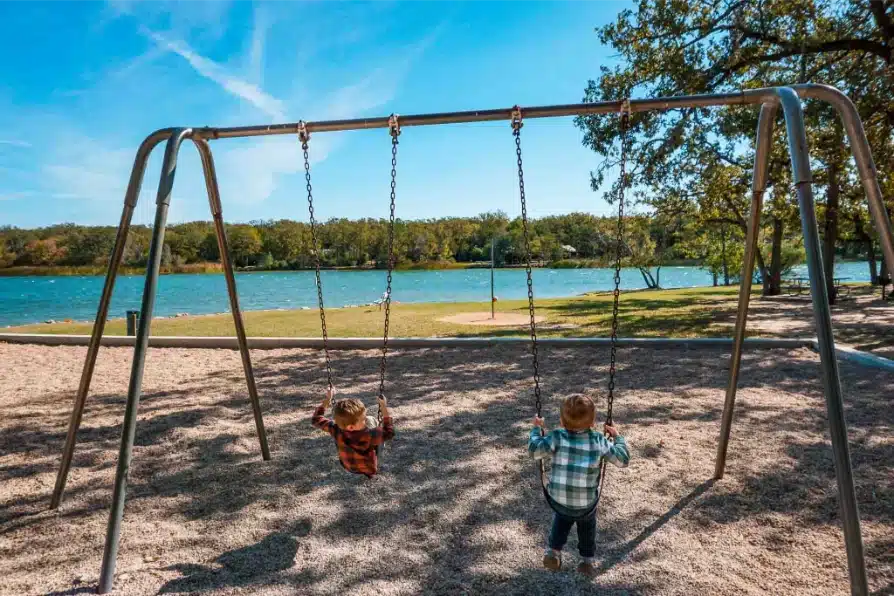 Two boys swinging on a swing set looking towards the lake at Lake Bastrop South Shore Park.