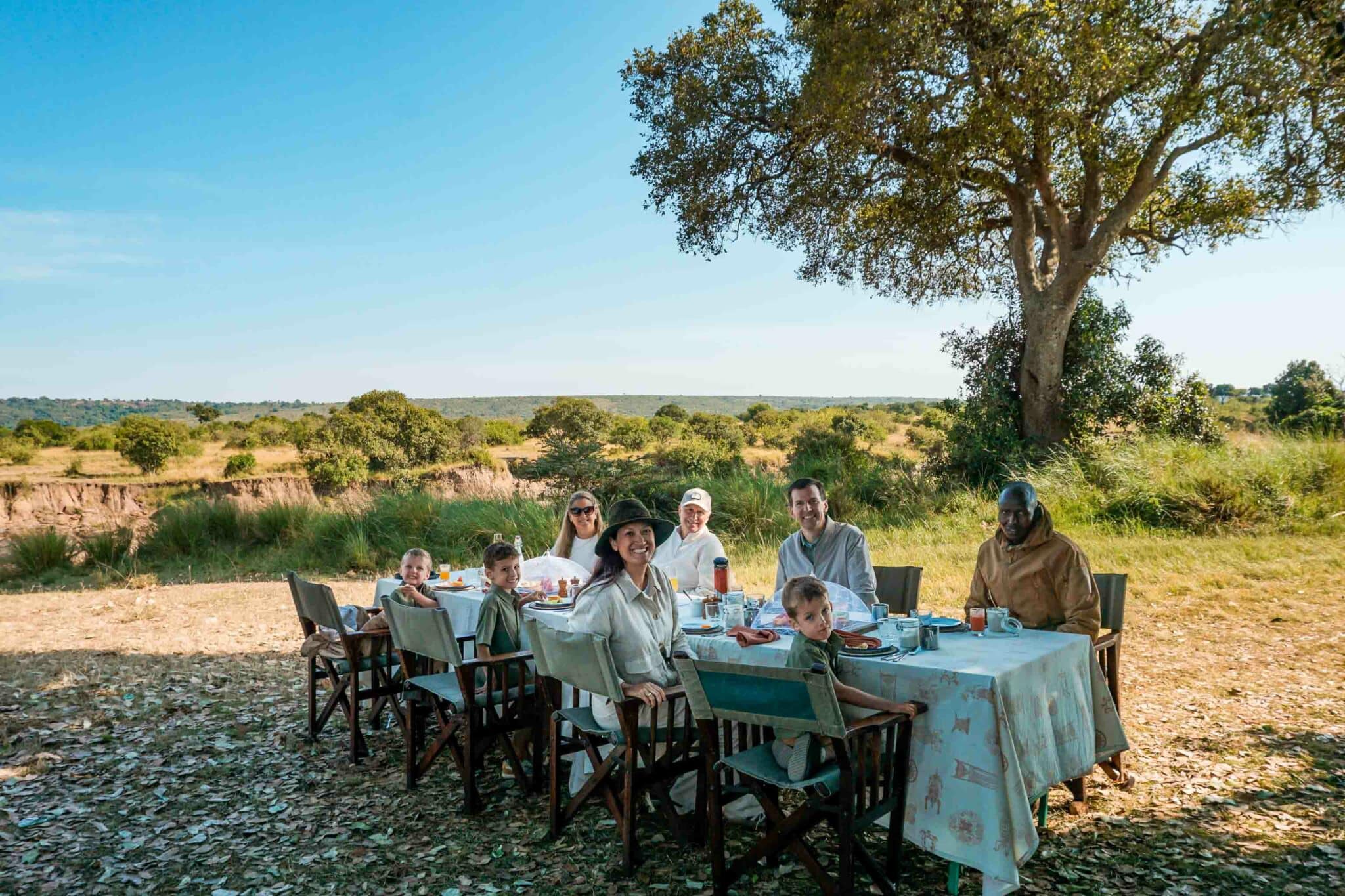 A family with three children, two parents, and two grandparents enjoying a bush breakfast with their Elewana safari guide in Maasai Mara North Conservancy.