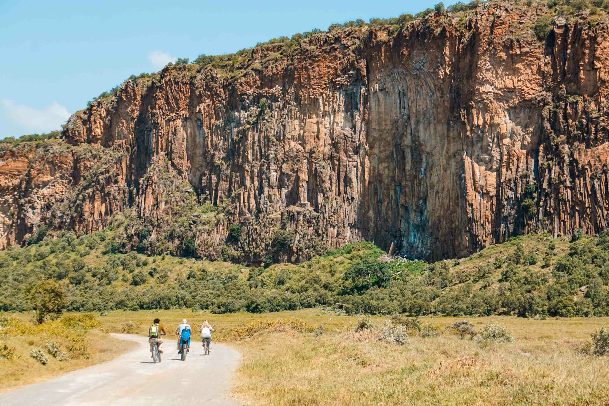 People riding bikes with a dramatic limestone cliff in the background at Hell's Gate National Park.